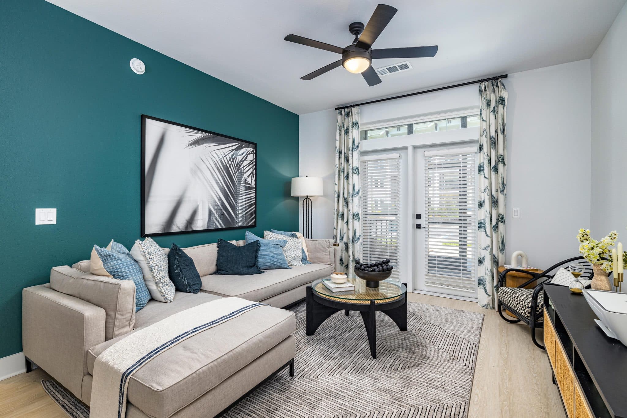 A modern furnished apartment living room with a ceiling fan, hardwood-style floors, and double doors leading outside.