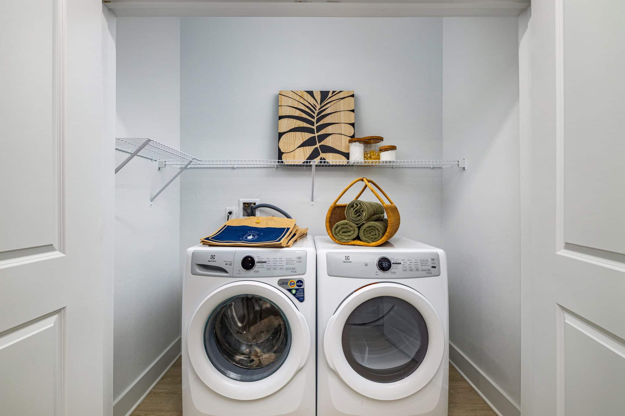 A laundry closet with two doors ajar showing an in-home washer and dryer and shelving inside.