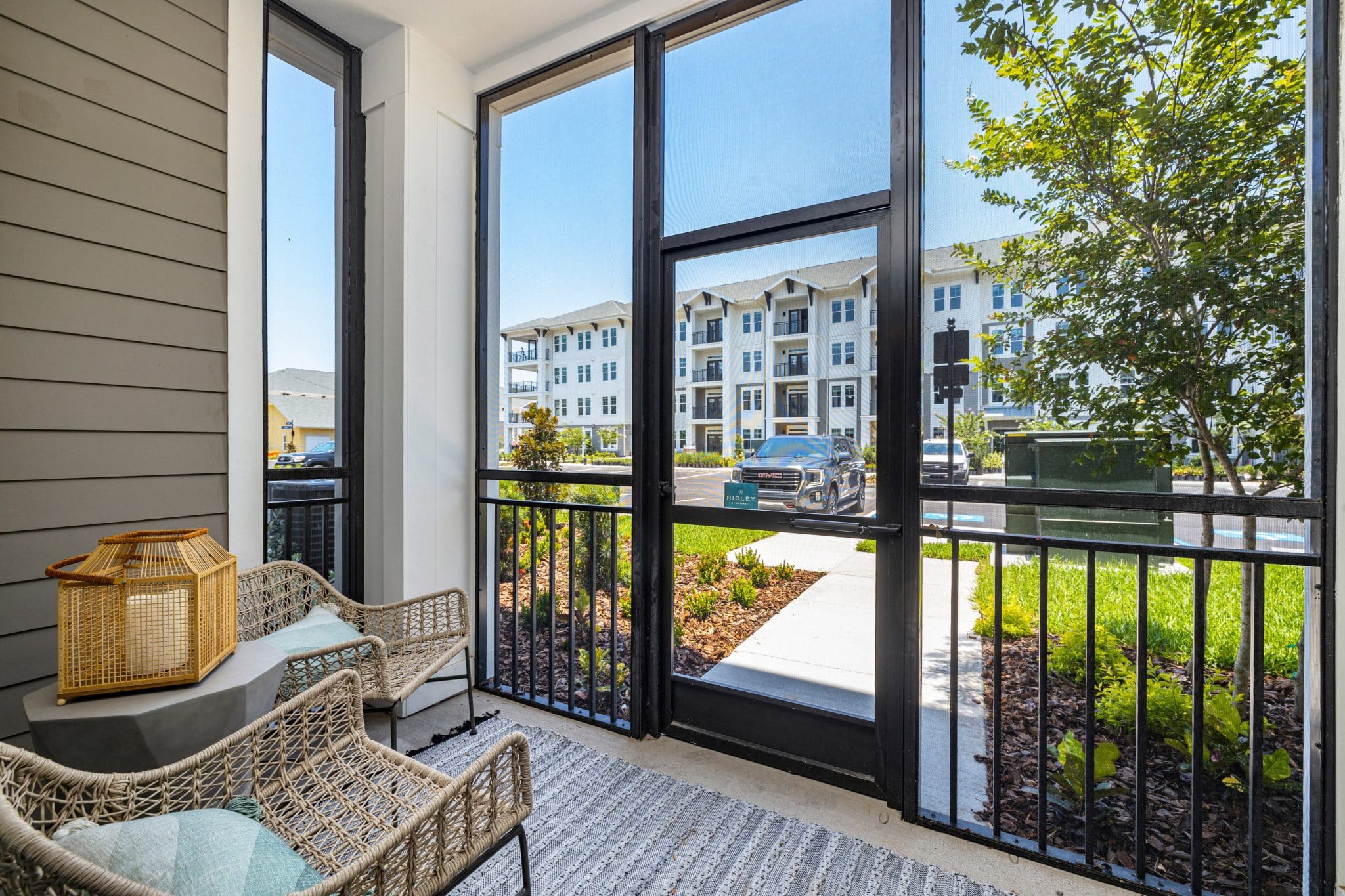 An enclosed, furnished outdoor patio with glass windows and doors near resident parking and beautiful landscaping.
