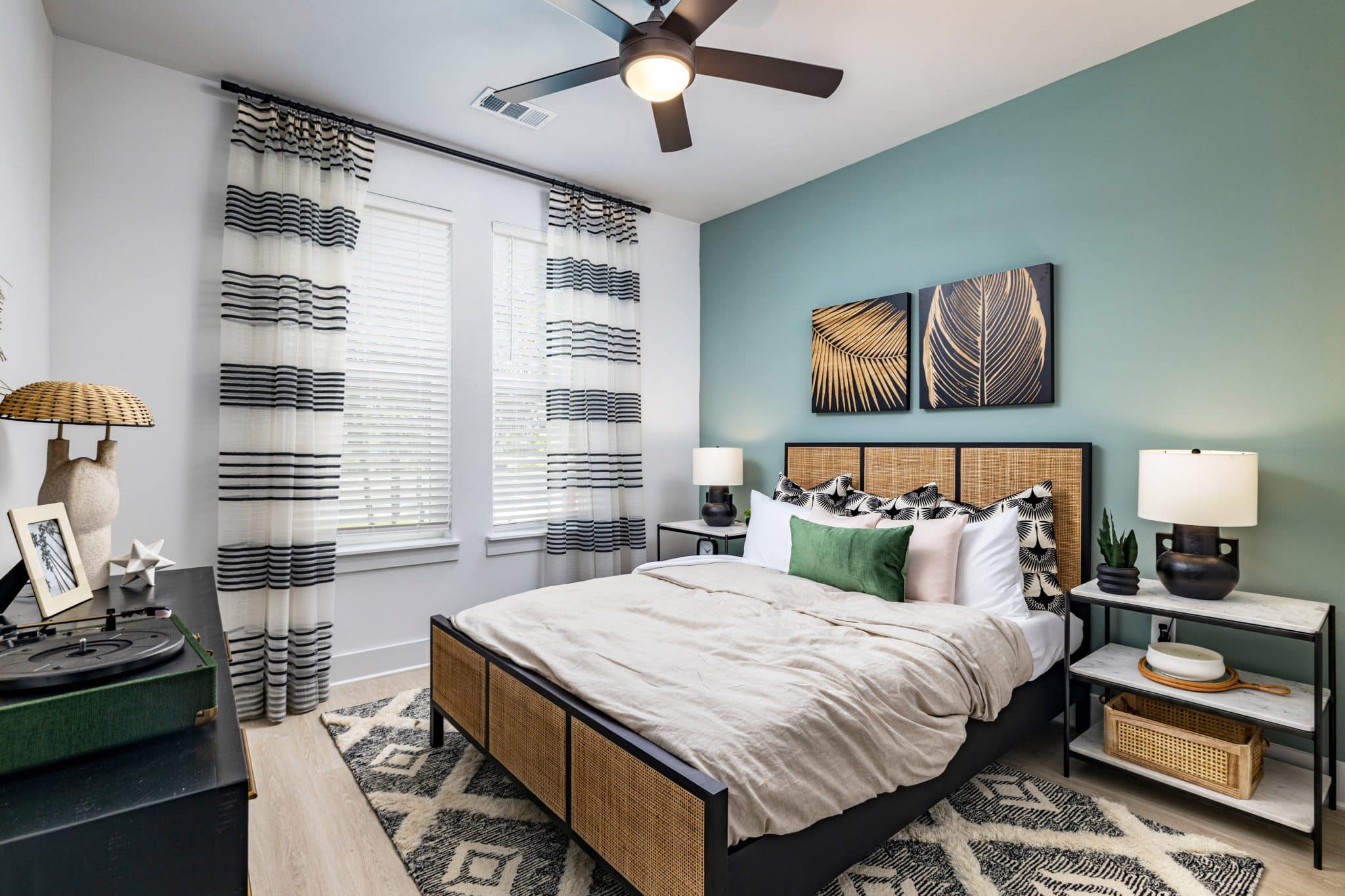 A bedroom with a ceiling fan, two windows, and hardwood-style flooring at Ridley at Waterset.