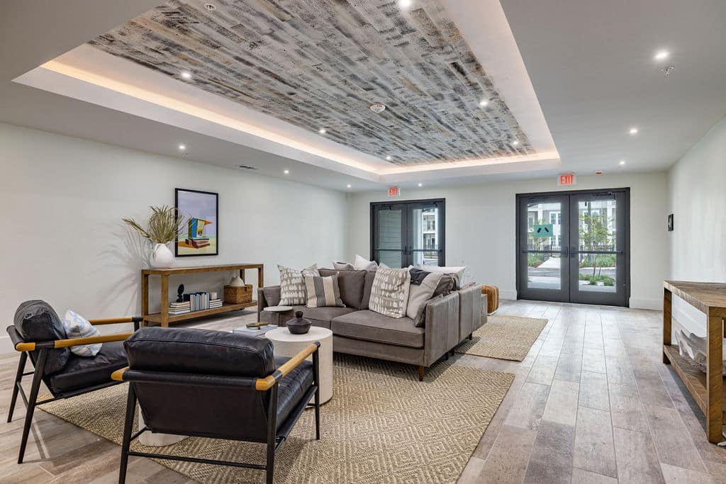 A community lounge with chairs, sofas, and tables in Ridley at Waterset's clubhouse with double doors leading outside.