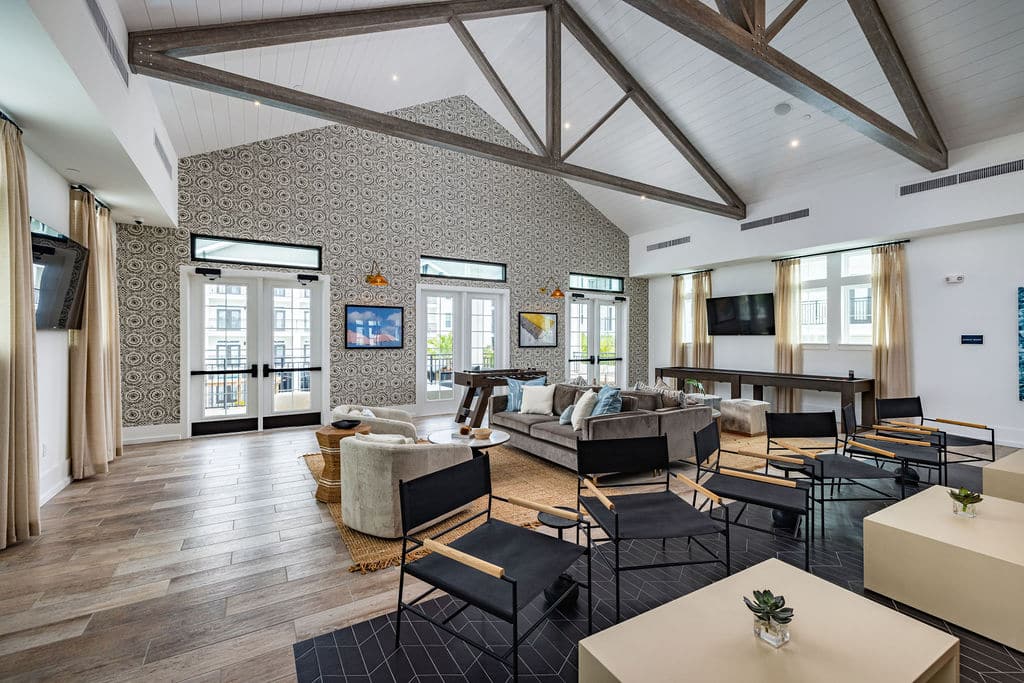 Ridley at Waterset's clubhouse with 3 double door entries leading into a room with several seating areas, TVs, and windows.