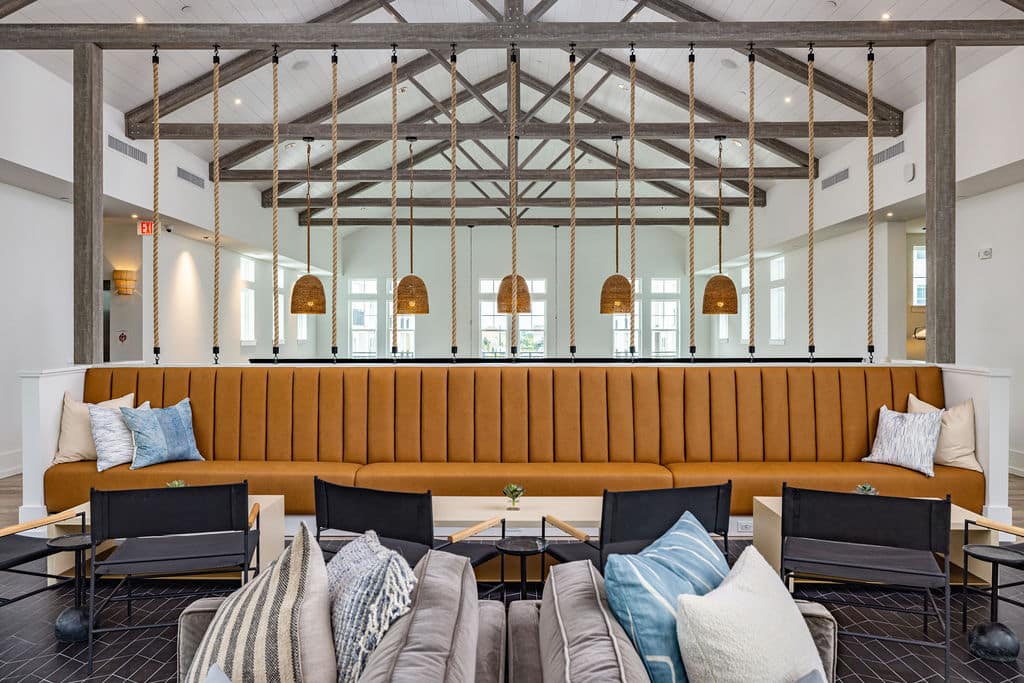 A community clubhouse with a seating area containing a long plush bench, chairs, and hanging lights.
