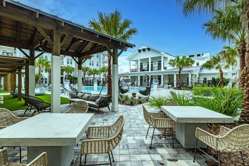 An outdoor space with tables, chairs, and palm trees near cabanas and a resort-style pool at Ridley at Waterset.