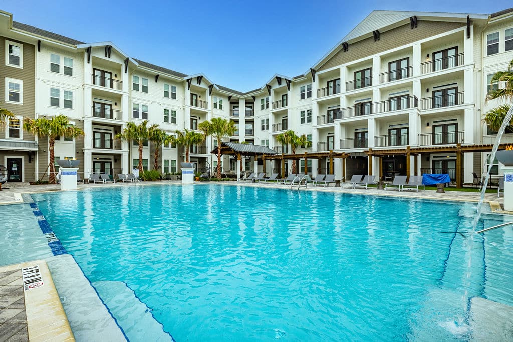 A spacious pool surrounded by lounge chairs, palm trees, and apartment buildings at Ridley at Waterset.
