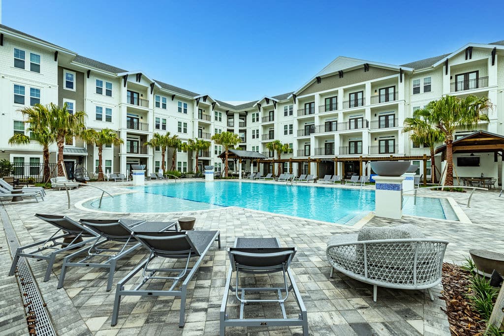 A resort-stye pool with lounge chairs, fountains, and palm trees surrounded by Ridley at Waterset's apartment buildings.
