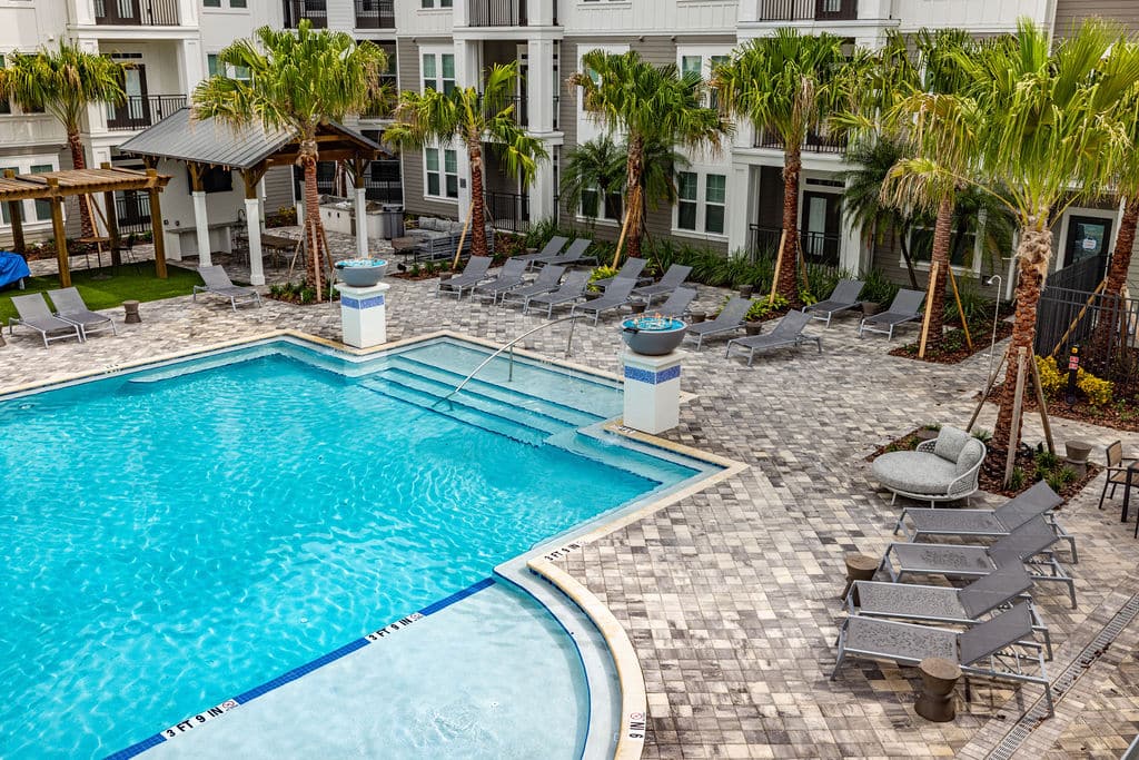 An aerial view of a resort-style pool, sundeck, lounge chairs, and palm trees at Ridley at Waterset.