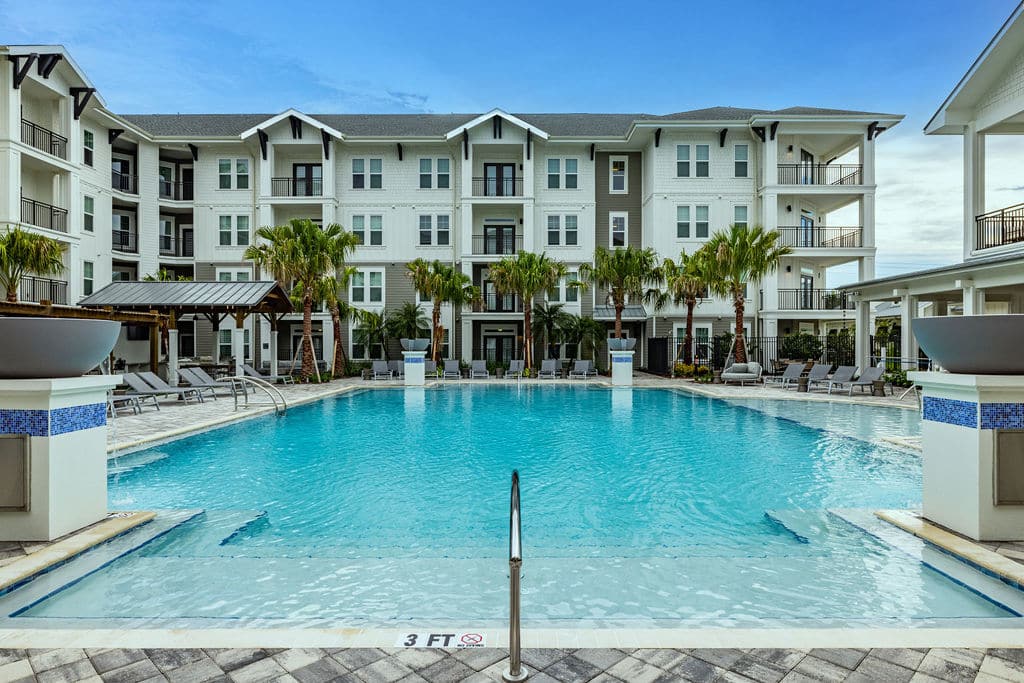 Ridley at Waterset's resort-style swimming pool with lounge chairs and palm trees surrounded by apartments with balconies.