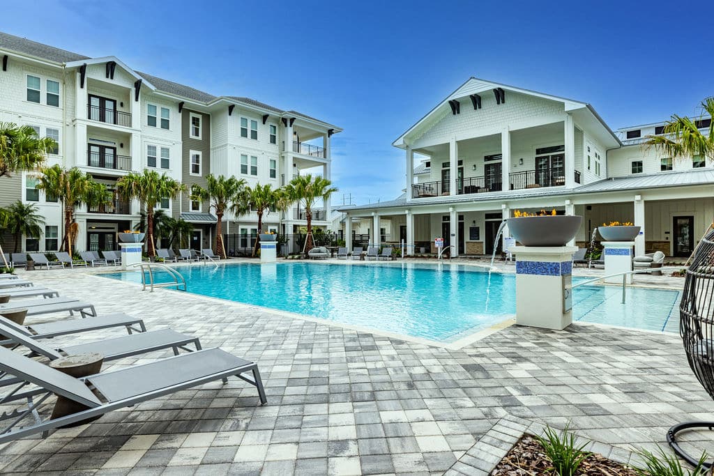 A large pool and sundeck with lounge chairs, palm trees, and apartments at Ridley at Waterset.